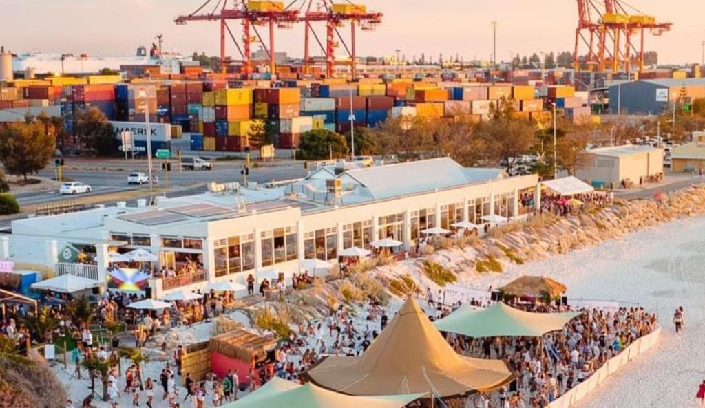 Aerial photo of COAST Port Beach with stacks of shipping containers in the background, and a mini festival set up in the foreground